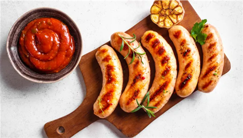 row of grilled sausages on cutting board with dipping sauce in bowl on the side